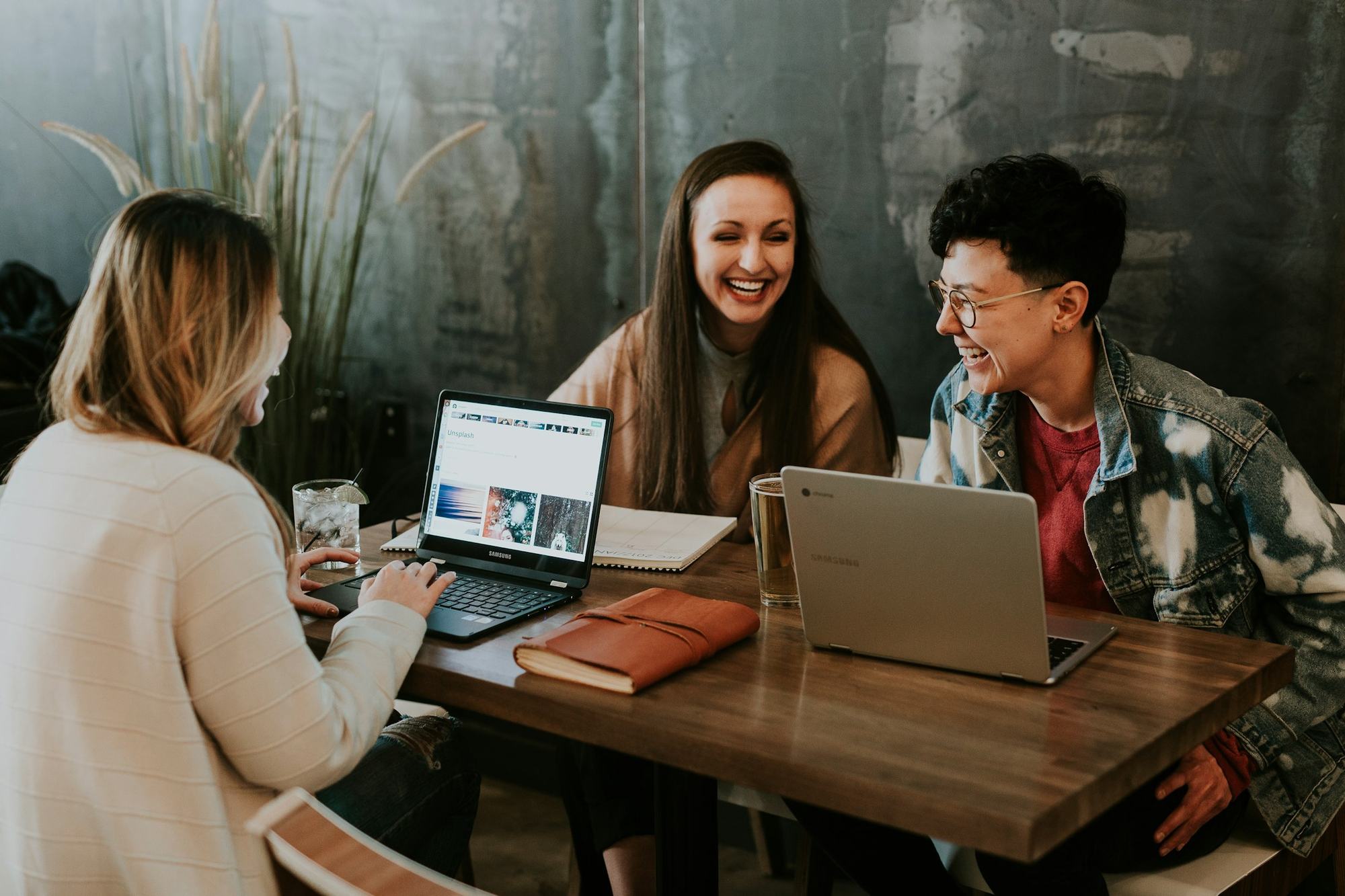 Three colleagues laughing together around laptops at a table